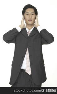 An asian businessman covers his ears with his hands