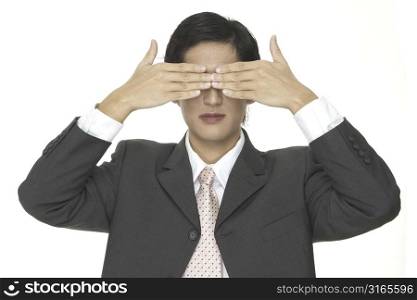 An asian businessman covers his eyes with his hands