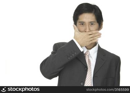 An asian businessman in a grey suit with his hand across his mouth