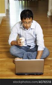 An asian businessman sitting on the floor and working on his laptop at home