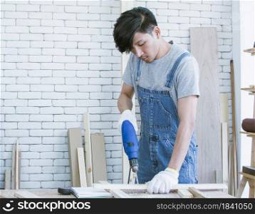 An asian carpenter using drill machine to make a hold on wood