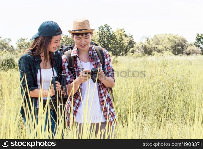 An asian couple traveling and hiking with backpacks together in summer time while standing in green field