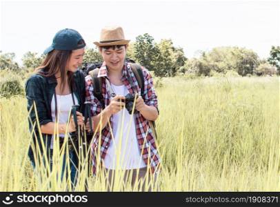 An asian couple traveling and hiking with backpacks together in summer time while standing in green field