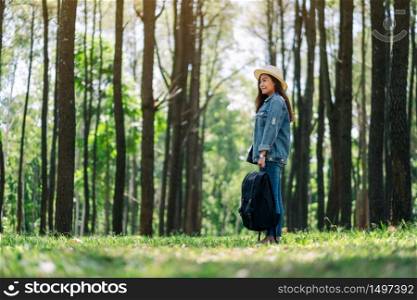 An asian female traveler with a hat and backpack looking into a beautiful pine woods