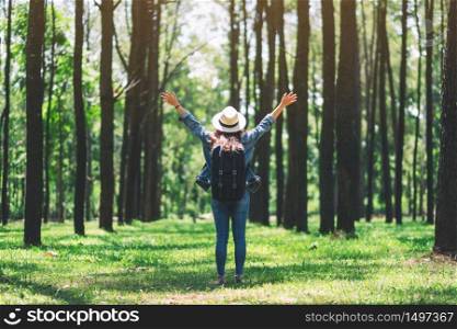 An asian female traveler with a hat and backpack standing back and open arms in a beautiful pine woods