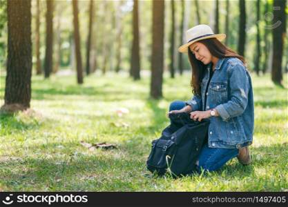 An asian female traveler with a hat opening her backpack while traveling in a beautiful pine woods