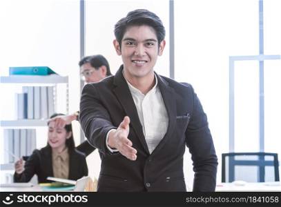 An asian handsome business man is extending his hand at camera for greeting