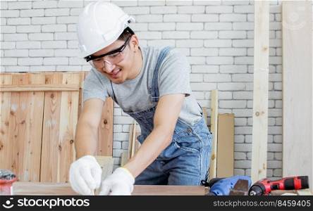 An asian handsome carpenter is measuring wood for making craft furniture