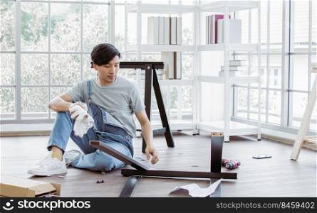 An asian handsome man is making an assembly of a furniture at home. Interior design and DIY Concept.