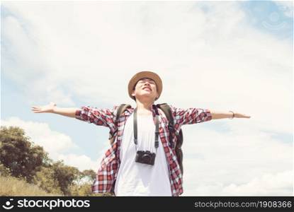 An Asian handsome man wearing hat, check shirt, camera and backpack for traveling in summer time. He feels happy and refresh with background of blue sky and white clouds