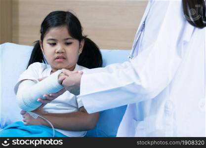 An asian little girl who got a cast on her arm because of accident, sitting on bed in hospital. Health and Insurance Concept.