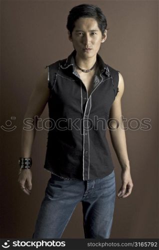 An asian male model in jeans and a waistcoat. Wearing a studded bracelet and other jewelry.