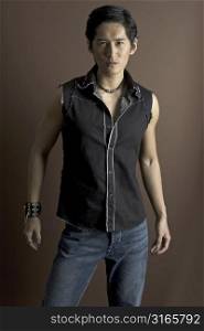 An asian male model in jeans and a waistcoat. Wearing a studded bracelet and other jewelry.