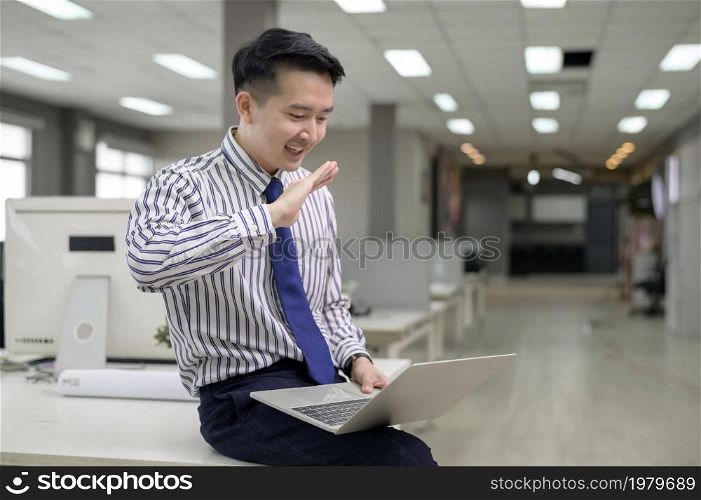 An Asian man is using laptop computer , video calling to business partner in office