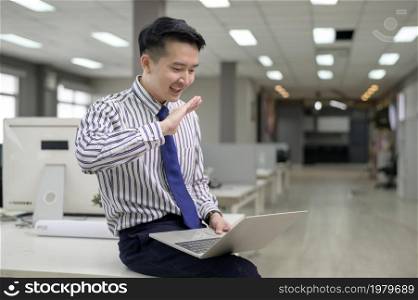 An Asian man is using laptop computer , video calling to business partner in office