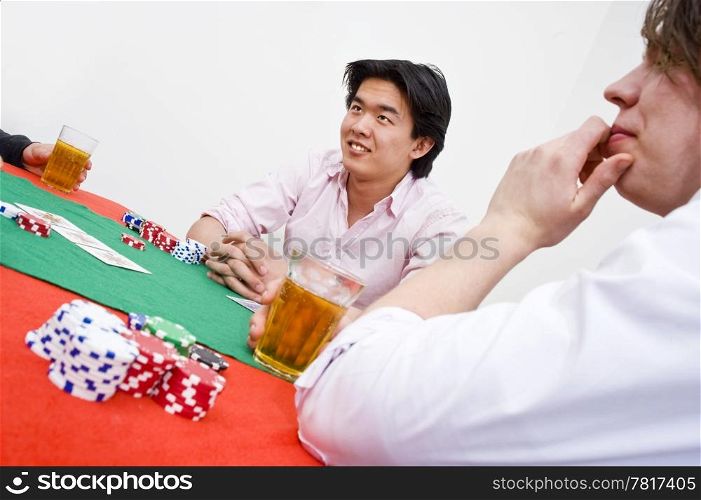 An Asian man sittingat the poker table during a game, ambiguously smiling at the competition