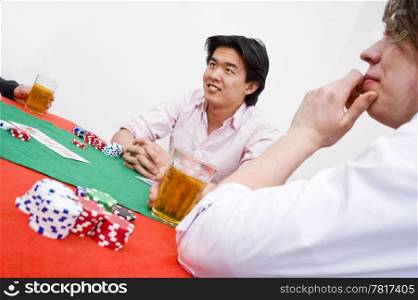 An Asian man sittingat the poker table during a game, ambiguously smiling at the competition