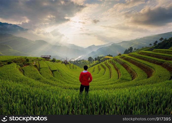 An Asian man watching at paddy rice terraces, agricultural fields in countryside of Mu Cang Chai, Yen Bai, mountain hills valley on summer in travel trip and holidays vacation concept, Vietnam.
