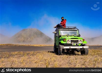 An Asian man wearing mask and sitting on jeep car at Mount Bromo. An active volcano, one of the most visited tourist attractions, in East Java on travel trip and holidays vacation, Indonesia.