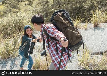 An asian man with backpack helping woman for climbing mountains by holding and pulling her hand. Travel and Summer Concept.