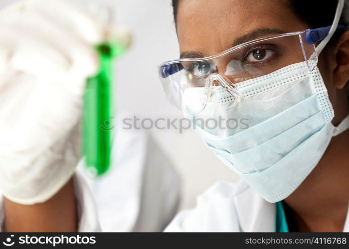 An Asian medical or scientific researcher or doctor looking at a test tube of green solution in a laboratory.