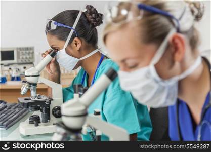 An Asian medical or scientific researcher or doctor using her microscope in a laboratory with her colleague out of focus next to her.