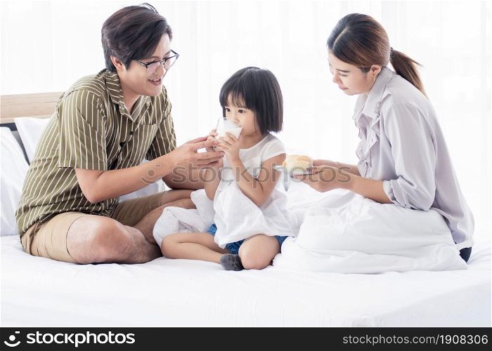 An asian parents serving breakfast and milk to their little daughter on bed in the morning