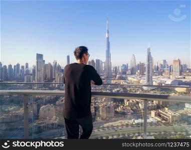 An Asian tourist man watching at Burj Khalifa in hotel, Dubai Downtown skyline, United Arab Emirates or UAE. Financial district in smart urban city in travel trip and holidays vacation concept.