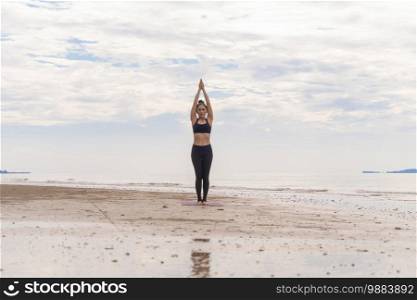 An Asian woman in yoga class club doing exercise and yoga at natural beach and sea coast outdoor in sport and recreation concept. People lifestyle activity.