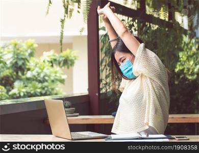 An asian woman is wearing mask to protect virus and using laptop for working at home in early morning