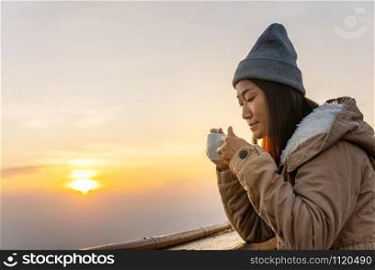 An Asian woman sits coffee at sunrise on the top of a mountain.