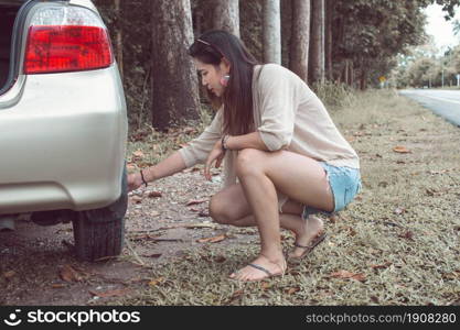 An asian woman trying to repair her broken car beside the street while traveling in holidays. Car Insurance and Summer holidays concept.