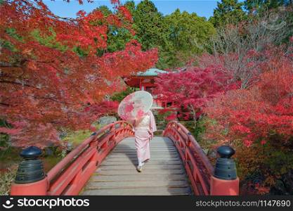 An Asian woman wearing Japanese traditional kimono standing in Daigoji Pagoda Temple with red maple leaves or fall foliage in autumn season. Colorful trees, Kyoto, Japan. Nature landscape background.