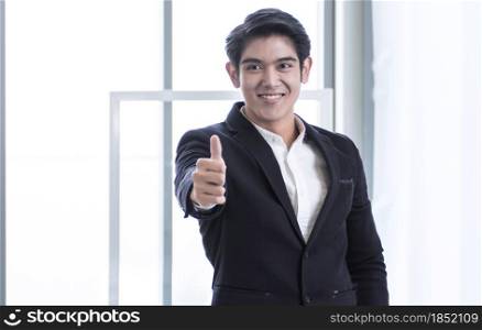 An Asian young business man wearing black formal black suit is successfully smiling and making thumb up