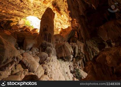 An Asian young man in casual wear stands and looks at the large stalagmite in the limestone cave. Koh Wua Ta Lap Island, Thailand. Focus on the stalagmite.