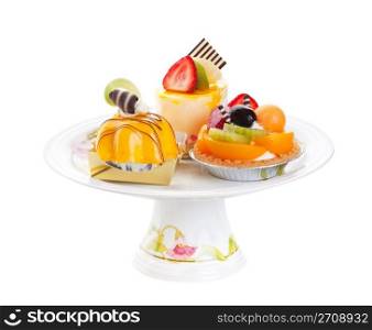 An assortment of Asian desserts, featuring (clockwise from top) Mousse Cake, Fruit Tart, and Mango Mousse. Displayed on a pedestal cake plate and shot on white background.
