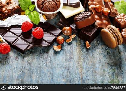 An assortment of white, dark, and milk chocolate with nuts, muffins, macaroons - on wooden background