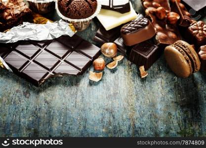 An assortment of white, dark, and milk chocolate with nuts, muffins, macaroons - on wooden background