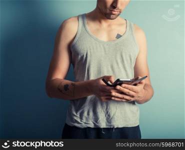 An athletic young man with tattoos wearing a vest is using a smart phone