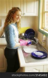An attractive blonde woman at home in the kitchen dong house hold chores.