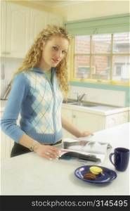 An attractive blonde woman relaxing at home in the kitchen reading a magazine.