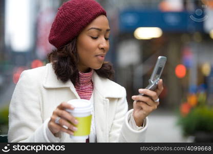 An attractive business woman checking her cell phone in the city. She could be text messaging or even browsing the web via wi-fi or a 3g connection.