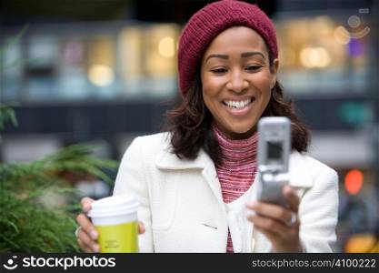An attractive business woman checking her cell phone in the city. She could be text messaging or even browsing the web via wi-fi or a 3g connection.