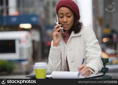 An attractive business woman talking on her cell phone and writing something down in her notes.