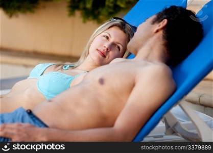 An attractive couple suntanning by a pool