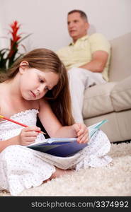 An attractive cute girl doing her homework with her father in the background