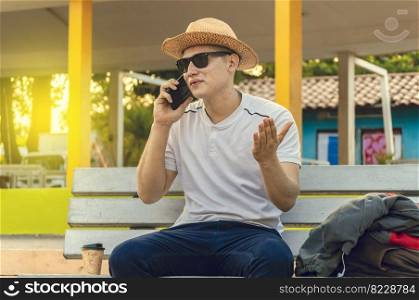 An attractive guy calling on a cell phone on a bench, a man sitting on a bench calling on the phone.