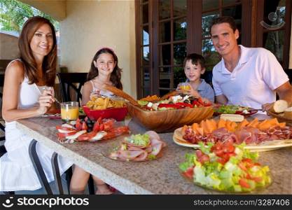 An attractive happy, smiling family of mother, father, son and daughter eating healthy food with ham, cheese and fresh salad at an outdoor table at home.