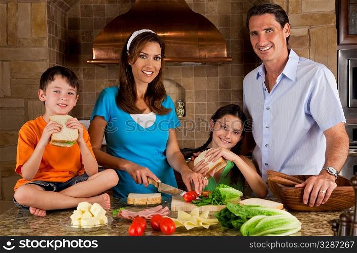 An attractive happy, smiling family of mother, father, son and daughter making healthy sandwiches with ham, cheese and fresh salad in a modern kitchen
