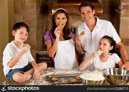 An attractive smiling family of mother, father, and two children baking and eating fresh chocolate chip cookies in a kitchen at home